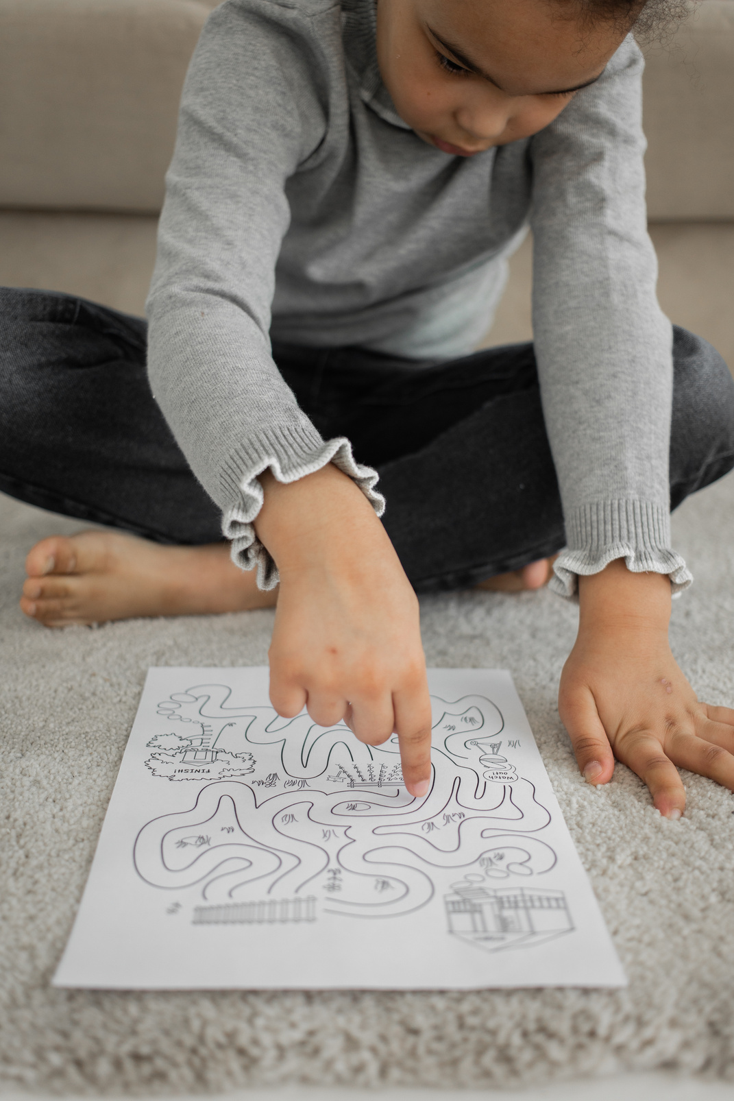 Serious little African American child solving labyrinth test on floor